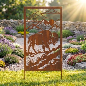May include: A rectangular metal garden screen with a rust-colored finish featuring a laser-cut design of a bison standing on a rocky landscape with mountains, a sun, and clouds in the background, supported by two thin metal stakes at the base.