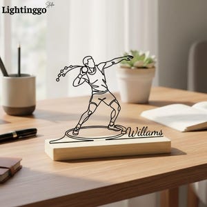 May include: A wooden desk ornament featuring a black line drawing of a shot put athlete in action. The athlete is depicted mid-throw, with the shot put in hand. The base of the ornament is rectangular, with the name "Willams" engraved on it.
