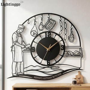 May include: Black metal wall clock with a butcher theme. The clock face is circular with gold hands. The design includes a butcher figure, hanging meats, and the text "ARTUR'S ARTISAN BUTCHER".