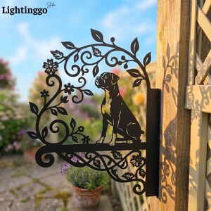 May include: Black metal dog sign featuring a Boxer silhouette within a floral and leaf design. The sign is mounted on a wooden post and includes the text "Lightinggo" in the upper left corner. The sign is designed for outdoor use.