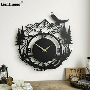 May include: Black metal wall clock with a nature-themed design. The clock features a mountain range, trees, and an eagle silhouette. The clock hands are gold. The clock is mounted on a white wall.