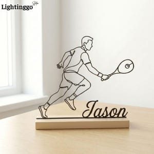 Puede incluir: Escultura de tenista en metal negro con el nombre "Jason" sobre una base de madera. La escultura representa a un tenista en movimiento, sosteniendo una raqueta. Es un artículo decorativo.