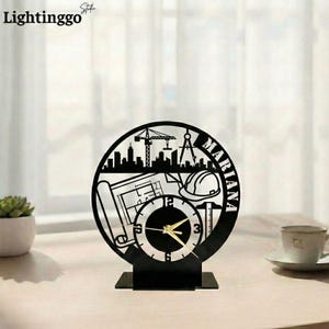Könnte beinhalten: Schwarze, lasergeschnittene Schreibtischuhr mit architektonischem Design, einschließlich Skyline, Bauplänen und Schutzhelm. Das Zifferblatt hat goldene Zeiger und der Name "Mariana" ist angezeigt. Die Uhr steht auf einem schwarzen Sockel.
