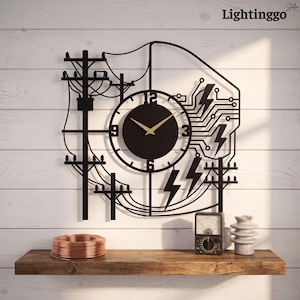 May include: A black wall clock featuring a central circular face with gold hands, surrounded by a metal cutout design of electrical utility poles, power lines, and lightning bolt symbols. The clock includes the text Lightinggo in the corner.