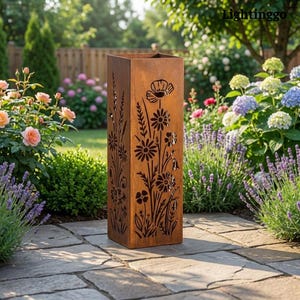 May include: A tall, rectangular garden sculpture made of weathered metal, featuring cut-out floral patterns. The sculpture has a rusty brown finish and is positioned on a stone patio. The background shows a vibrant garden with diverse flowers and foliage.