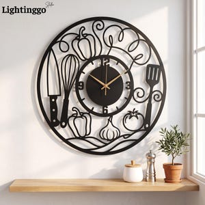 Peut inclure: Une horloge murale circulaire en métal noir avec un design découpé représentant des ustensiles de cuisine comme un couteau, un fouet et une spatule, ainsi que des légumes tels que poivrons, ail et tomate. Aiguilles dorées et chiffres noirs.