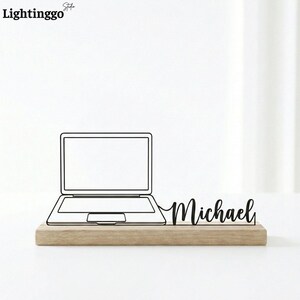 May include: A wooden desk tidy with a black outline of a laptop and the name "Michael" in a cursive font. The laptop design is connected to the name. The tidy is set on a light-coloured wooden base.