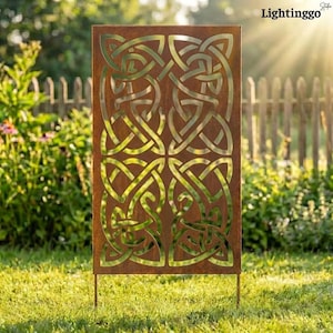 May include: A rectangular, weathered metal garden screen with a Celtic knot design. The screen is a rusty brown color and is supported by two metal legs. The background features green grass, a wooden fence, and sunlight.