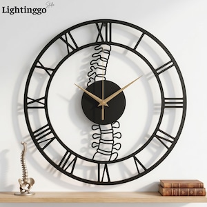 May include: Black metal wall clock with Roman numerals and gold hands. The clock features a unique design with a spine-shaped accent in the center. The clock is mounted on a white wall, with a wooden shelf below. The brand name "Lightinggo" is in the top left corner.