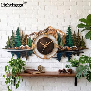 May include: A wall clock featuring a landscape of snow-capped mountains and evergreen trees reflected in water. The circular clock face is dark brown with gold-colored hands and numerals 3, 6, 9, and 12. The text Lightinggo Studio is visible.