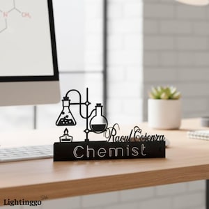Può includere: Un cartello da scrivania nero con un design di attrezzature da laboratorio chimico. Il cartello include il nome "Raoul Cosenza" e la parola "Chemist" in lettere bianche. Una candela e un pallone fanno anche parte del design.