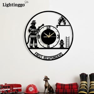 Puede incluir: Reloj de pared de metal negro con la silueta de un bombero, una esfera y el texto "FIRST RESPONDERS". El reloj incluye una boca de incendios, llamas y un diseño de escalera. Las manecillas del reloj son doradas.