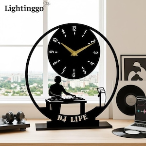 Könnte beinhalten: Schwarze DJ-Uhr mit rundem Zifferblatt und goldenen Zeigern. Die Uhr zeigt eine Silhouette eines DJs an einem Plattenspieler mit dem Text "DJ LIFE" am Sockel. Die Uhr ist etwa 30 cm hoch.