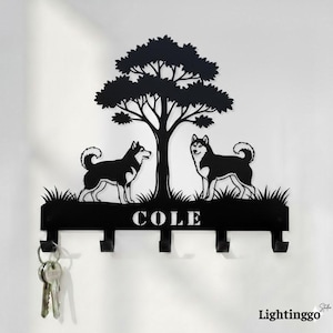 May include: Black metal key holder featuring two husky dogs under a tree silhouette. The key holder has four hooks and the name "COLE" is displayed. The key holder is mounted on a white wall.