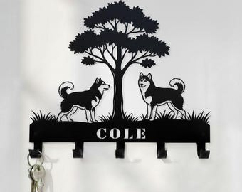 May include: Black metal key holder with a tree and two husky dog silhouettes. The key holder has four hooks and the name "COLE". The key holder is mounted on a white wall.