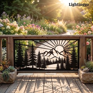 May include: A black metal decorative panel featuring a laser-cut design of a mountain range, a rising sun with radiating beams, and a dense forest of pine trees. The rectangular panel is mounted within a wooden frame on a deck.