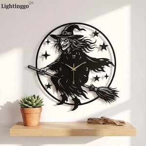 May include: A circular black wall clock featuring a cutout design of a witch flying on a broomstick surrounded by stars. The clock face has gold-colored hands and numerical markers at the 12, 3, 6, and 9 positions, set against a plain wall.