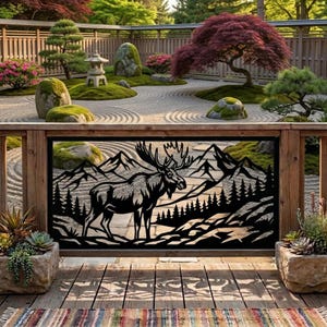May include: A black metal decorative panel featuring a laser-cut silhouette of a moose standing in a forest with mountains in the background. The rectangular panel is mounted within a wooden frame, showcasing intricate cutouts of trees and peaks.