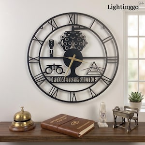 May include: A black metal wall clock featuring Roman numerals and optometry-themed silhouettes including a phoropter, trial frame, and prism. The center of the clock displays the text OPTOMETRY PRACTICE with gold-colored hour and minute hands.