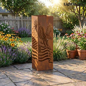 Puede incluir: Una escultura de jardín alta y rectangular de metal envejecido. El diseño presenta un recorte detallado de una bandera estadounidense y un águila volando. La escultura está colocada en un patio de piedra, rodeada de un jardín con flores coloridas.