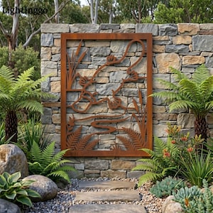 May include: A rectangular, rust-colored metal wall art piece depicting a pond scene with cattails, ferns, and a frog. The artwork is mounted on a natural stone wall, surrounded by lush greenery, creating a serene outdoor aesthetic.