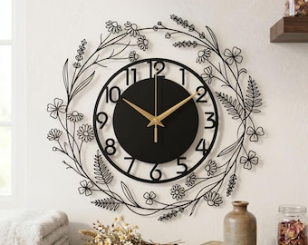 May include: Black wall clock with gold hands and a floral wreath design. The clock face is black with gold hands and black numerals. The floral wreath is made of black metal and features flowers and leaves. The clock measures approximately 12 inches in diameter.