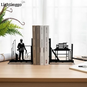 May include: A pair of black metal bookends featuring silhouettes of an engineer holding a blueprint and a compass on the left, and a multi-storey building structure on the right, supporting four books titled Engineering and Masting.