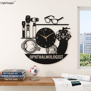 May include: A black wall clock featuring an ophthalmology theme with silhouettes of medical instruments, eyeglasses, and an eye diagram. The clock face has gold hands and the word OPHTHALMOLOGIST is cut out at the bottom of the circular frame.