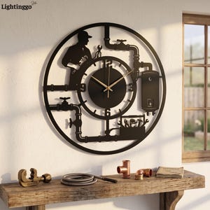 May include: A circular black wall clock featuring a silhouette of a plumber holding a wrench, integrated with pipework, a water heater, and a toolbox. The clock face has a solid black center with gold-colored hands and white numerals 3, 6, 9, and 12.