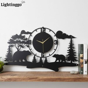 Puede incluir: Reloj de pared de metal negro con un diseño de silueta de oso y bosque. El reloj tiene una esfera redonda con manecillas doradas y un borde decorativo con árboles, nubes y osos. El texto "Lightinggo" es visible.