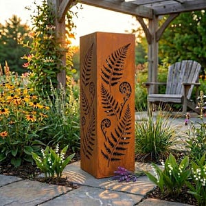 Può includere: Un'alta scultura da giardino rettangolare in metallo usurato con intagli a forma di foglie di felce. La scultura è di colore marrone ruggine e si trova in un giardino con fiori e un pergolato in legno sullo sfondo.