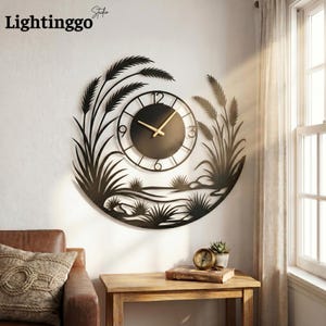 Puede incluir: Reloj de pared de metal negro con un diseño circular que presenta una esfera y siluetas decorativas de plantas. El reloj tiene manecillas doradas. El texto "Lightinggo" está en la esquina superior izquierda.