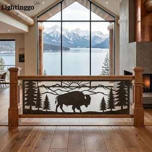 May include: A dark metal railing insert featuring a laser-cut silhouette of a bison standing in front of a mountain range, a rising sun, and evergreen trees. The decorative panel is framed by two vertical wooden posts on a wooden floor.