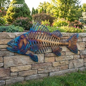 Op de afbeelding: Een metalen wanddecoratie in de vorm van een vissenskelet met een hittebehandelde afwerking in iriserende blauwe, paarse en koperen tinten. Het uitgesneden ontwerp toont een gedetailleerde kop, vinnen en een skeletachtige ribstructuur.