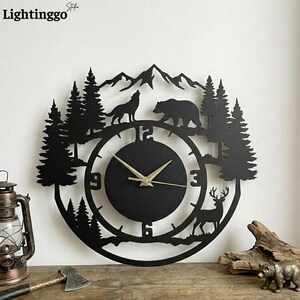 May include: Black metal wall clock featuring a forest scene with a wolf, bear, deer, and trees. The clock has a circular face with gold-colored hands and the numbers 3, 6, 9, and 12. The clock is approximately 12 inches in diameter.