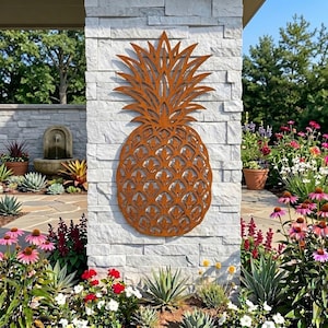 Puede incluir: Una pieza de arte mural de metal color óxido con forma de piña y un detallado patrón de celosía cortado con láser. La piña presenta una corona puntiaguda texturizada y un cuerpo redondeado con recortes en forma de hoja en todo el diseño.