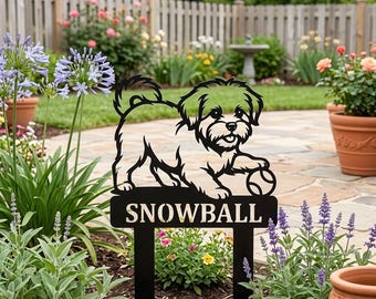 May include: Black metal garden stake featuring a dog design with the name "SNOWBALL". The dog is depicted with a ball, and the stake is placed in a garden setting with flowers and greenery.