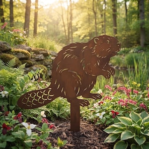 May include: A flat, rust-coloured metal garden stake shaped like a beaver. The silhouette features cut-out details representing fur texture and the characteristic scaly pattern on the wide, flat tail. The figure is mounted on a vertical metal post.