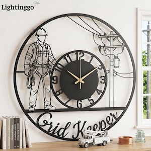 May include: A circular black metal wall clock featuring a silhouette of a utility worker in a hard hat and harness, a utility pole with power lines, and the text Grid Keeper. The clock face has large cut-out numbers and gold-colored hands.
