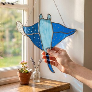 May include: A stained glass stingray suncatcher in shades of blue, with white polka dots and a light blue center. The suncatcher is hanging by a silver chain. The word "Lightinggo" is visible in the top left corner.