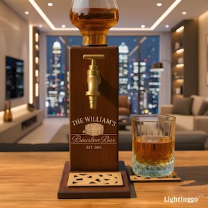 Op de afbeelding: Een houten bourbon dispenser met een messing kraan en een glazen karaf. De dispenser is gegraveerd met "The William's Bourbon Bar" en "EST. 2015". Een glas bourbon staat op een houten onderzetter.