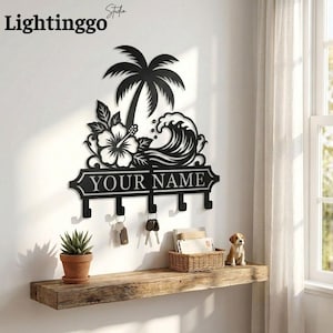May include: Black metal key holder featuring a tropical design with a palm tree, hibiscus flower, and wave. The key holder has hooks and the text "YOUR NAME". A small potted plant, keys, and a basket are on a wooden shelf below.