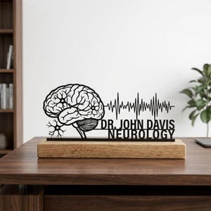 Könnte beinhalten: Ein schwarzes, lasergeschnittenes Holz-Schreibtischschild mit einer Gehirnillustration, einer EKG-Linie und dem Text "DR. JOHN DAVIS NEUROLOGY". Das Schild ist auf einem rechteckigen Holzsockel montiert. Der Hintergrund ist eine verschwommene Büroumgebung.