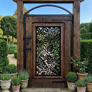 May include: A rustic wooden gate featuring a central black metal panel with an intricate laser-cut leaf and vine pattern. The gate is framed by thick, weathered timber posts and topped with a curved metal arch, set within a garden landscape.