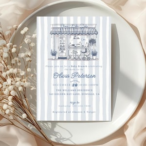 May include: A baby brunch invitation card with a blue and white striped background. The card features an illustration of a shop with a stroller and text that reads "Olivia Petersen" and event details. The card is on a white plate with white flowers.