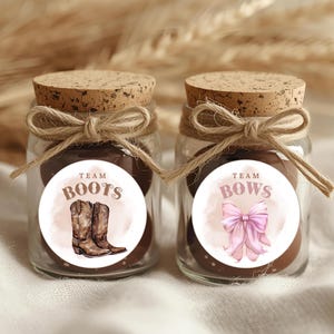 May include: Two small glass jars with cork lids and twine bows. Each jar has a round label. One says "Team Boots" with a watercolor image of cowboy boots. The other says "Team Bows" with a pink bow.