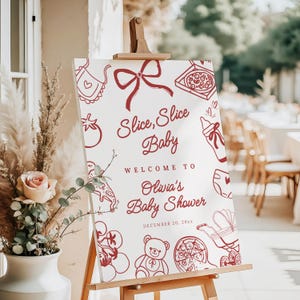 May include: A white sign on a wooden easel with burgundy illustrations and text. The sign reads "Slice, Slice Baby" and welcomes guests to Olivia's Baby Shower, scheduled for December 20, 20xx. The sign is decorated with baby-themed illustrations.