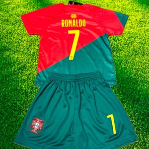 May include: A red and green soccer uniform set. The jersey has the name "RONALDO" and the number "7" in yellow. The shorts are green with the number "1" in yellow and a crest.