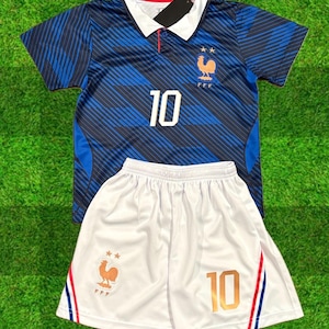 Puede incluir: Una camiseta de fútbol a rayas azules y azul oscuro con cuello blanco, el número 10 y un emblema de gallo dorado, junto con pantalones cortos de fútbol blancos con el número 10, un emblema de gallo dorado y rayas laterales rojas, blancas y azules.