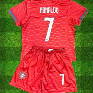 May include: A red soccer jersey and shorts set. The jersey has the name "RONALDO" and the number "7" on the back. The shorts also feature the number "7" and a crest. The set has teal accents.